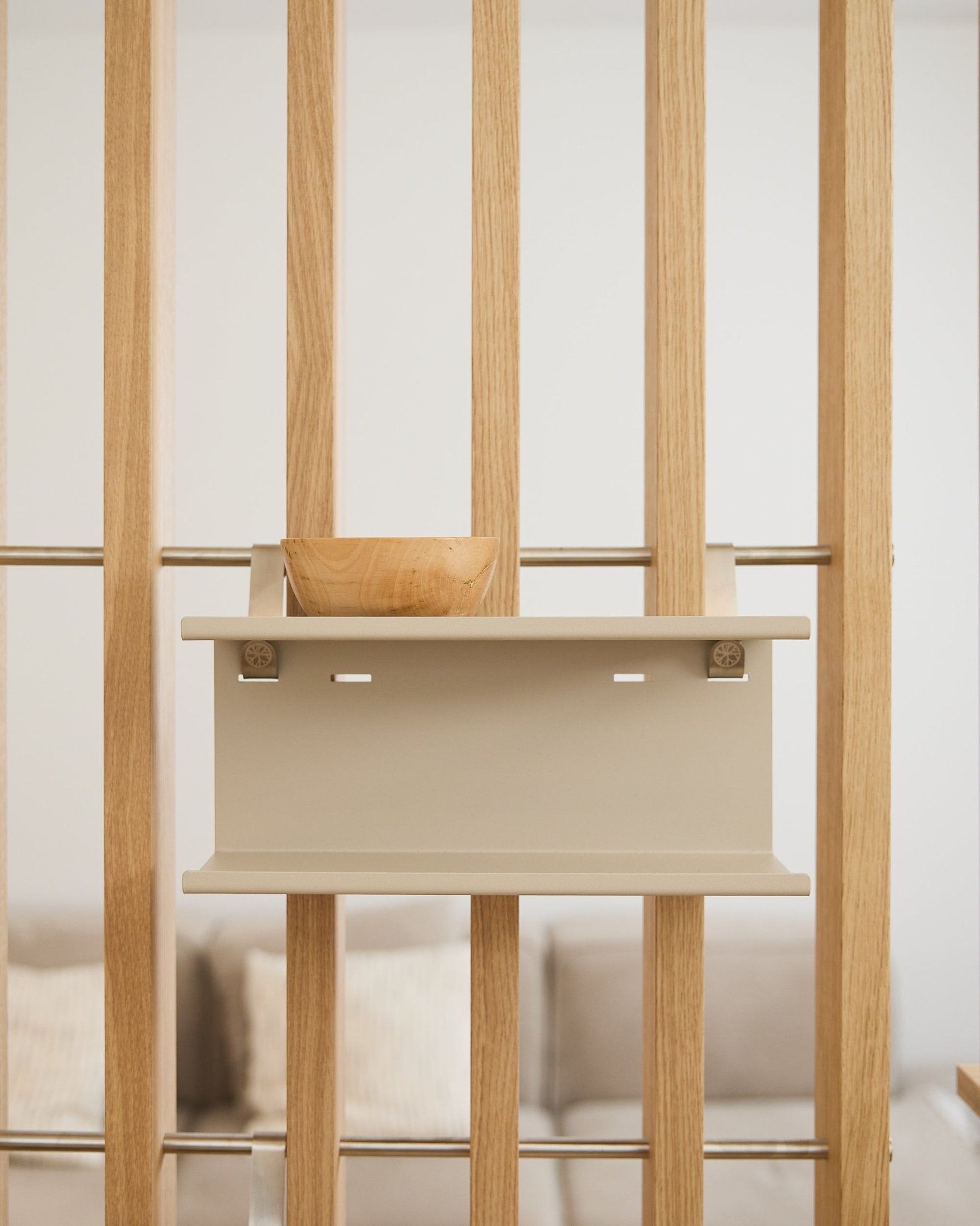 En small træskål på beige Nell Double Metal Shelf fra WoodUpp (31,7 cm), med en sløret sofa og puder i baggrunden.