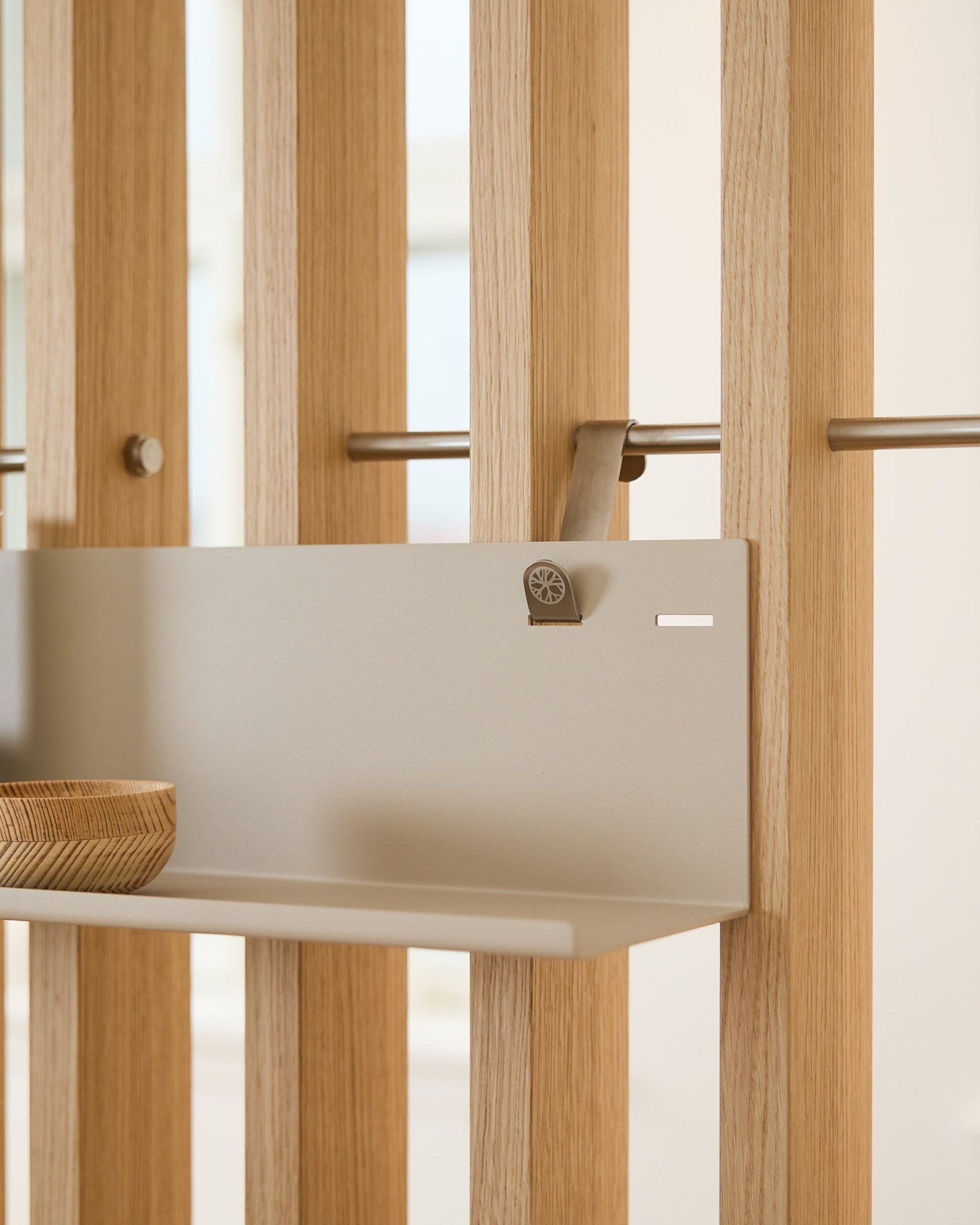 Beige WoodUpp BM1 metalhylde (63 x 13,4 cm) monteret på vertical akustisk lamelvægspanel, med en træskål på venstre side af hylden.