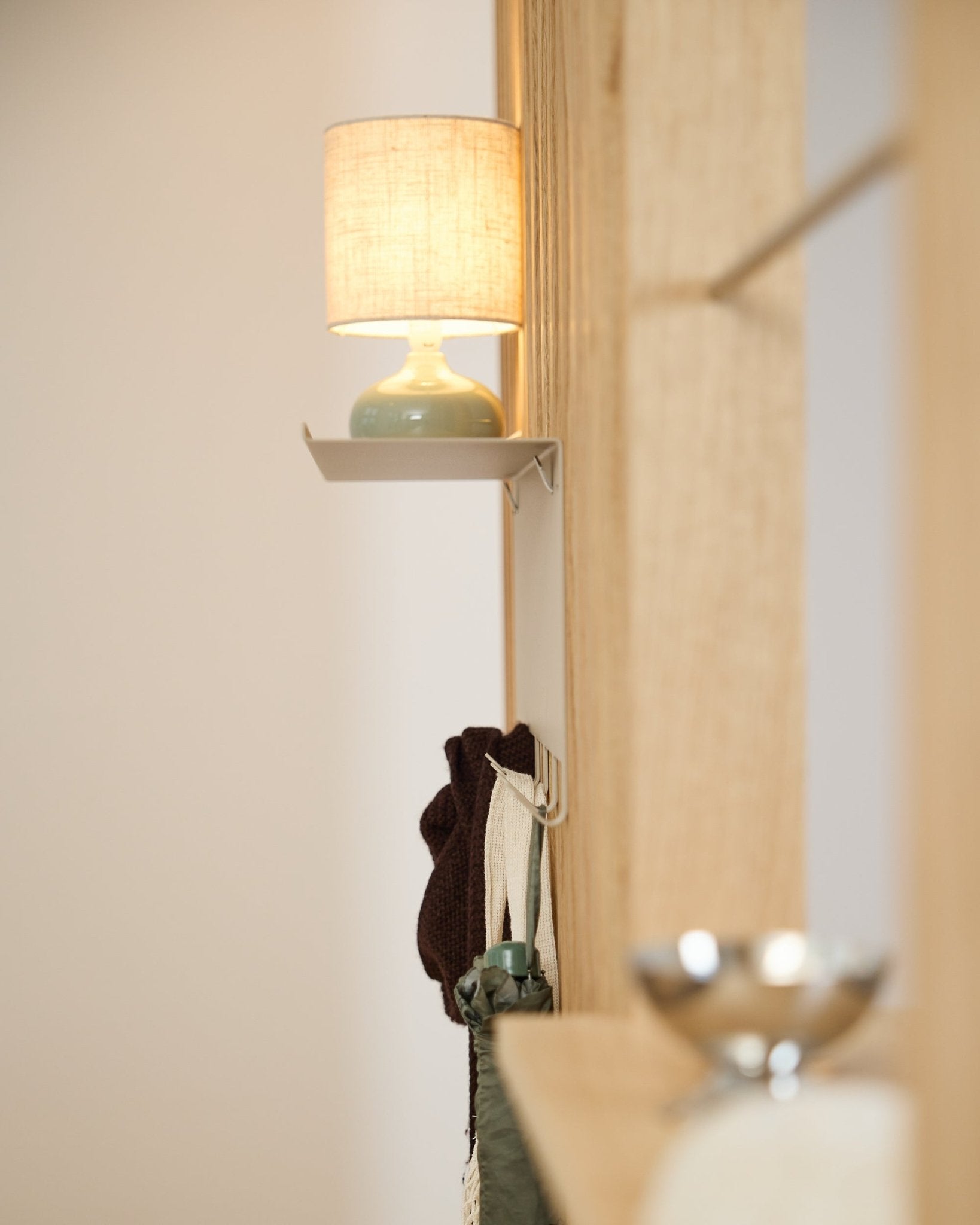 En beige WoodUpp Nell knagerække BM1 (63,5 x 24 cm) står under en small bordlampe ved siden af en væg i lyst nordisk træ Akustikpanel.