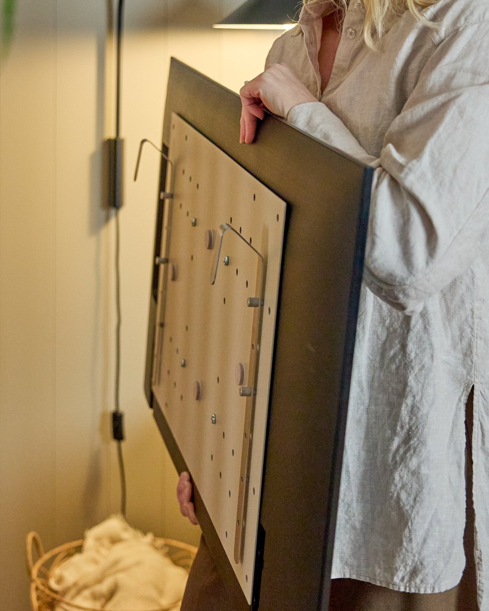 En person i en lys skjorte holder WoodUpp Nell BM1 TV-Mount i beige, 64x44 cm — kompatibel med nordiske akustiske træpaneler, til installationer uden væg.