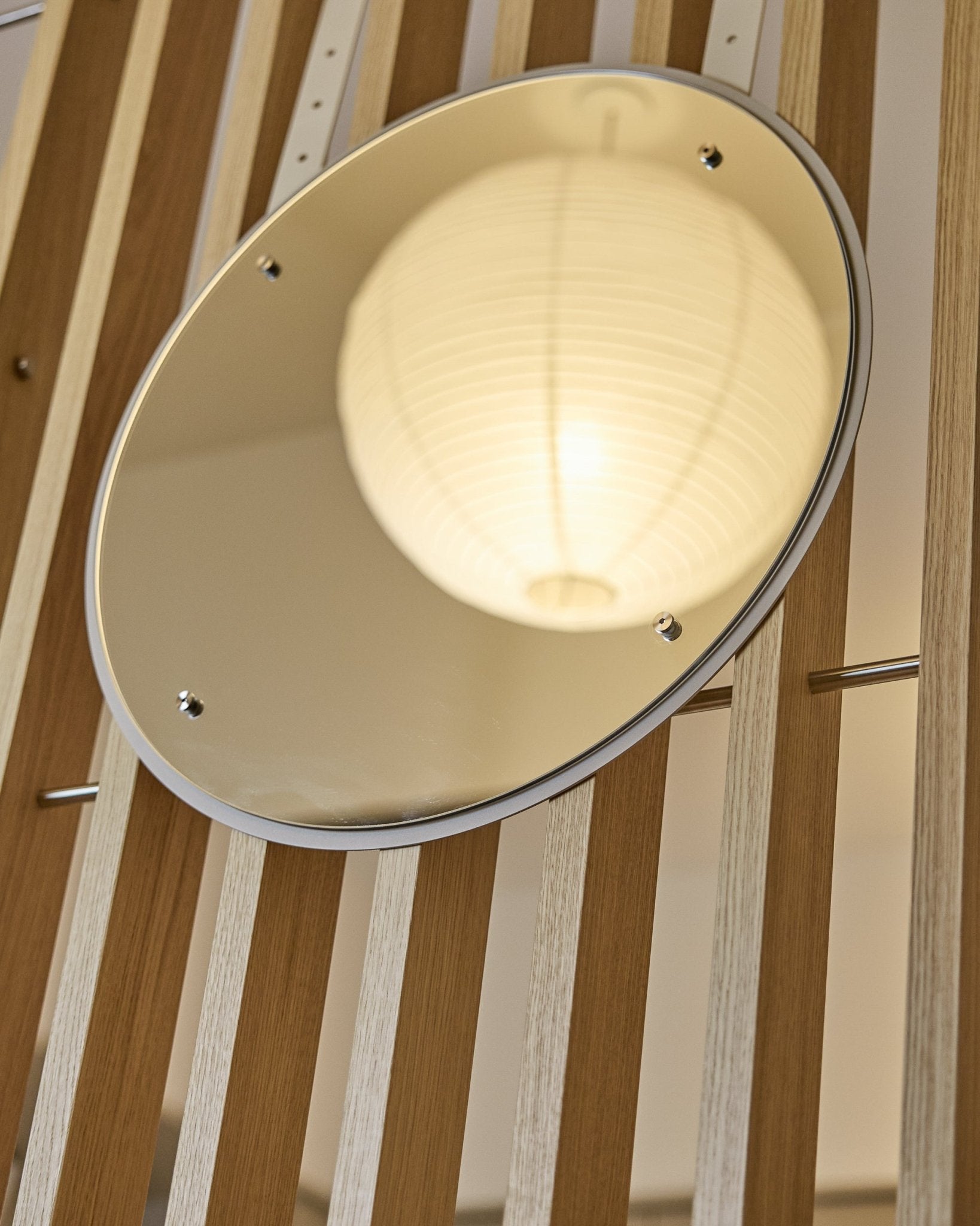 Vala | Mirror / BM1, D54 cm fra WoodUpp er et højdejusterbart rundt spejl monteret på vertical akustiske lamelvægspaneler, som reflekterer en glødende papirlanterne.
