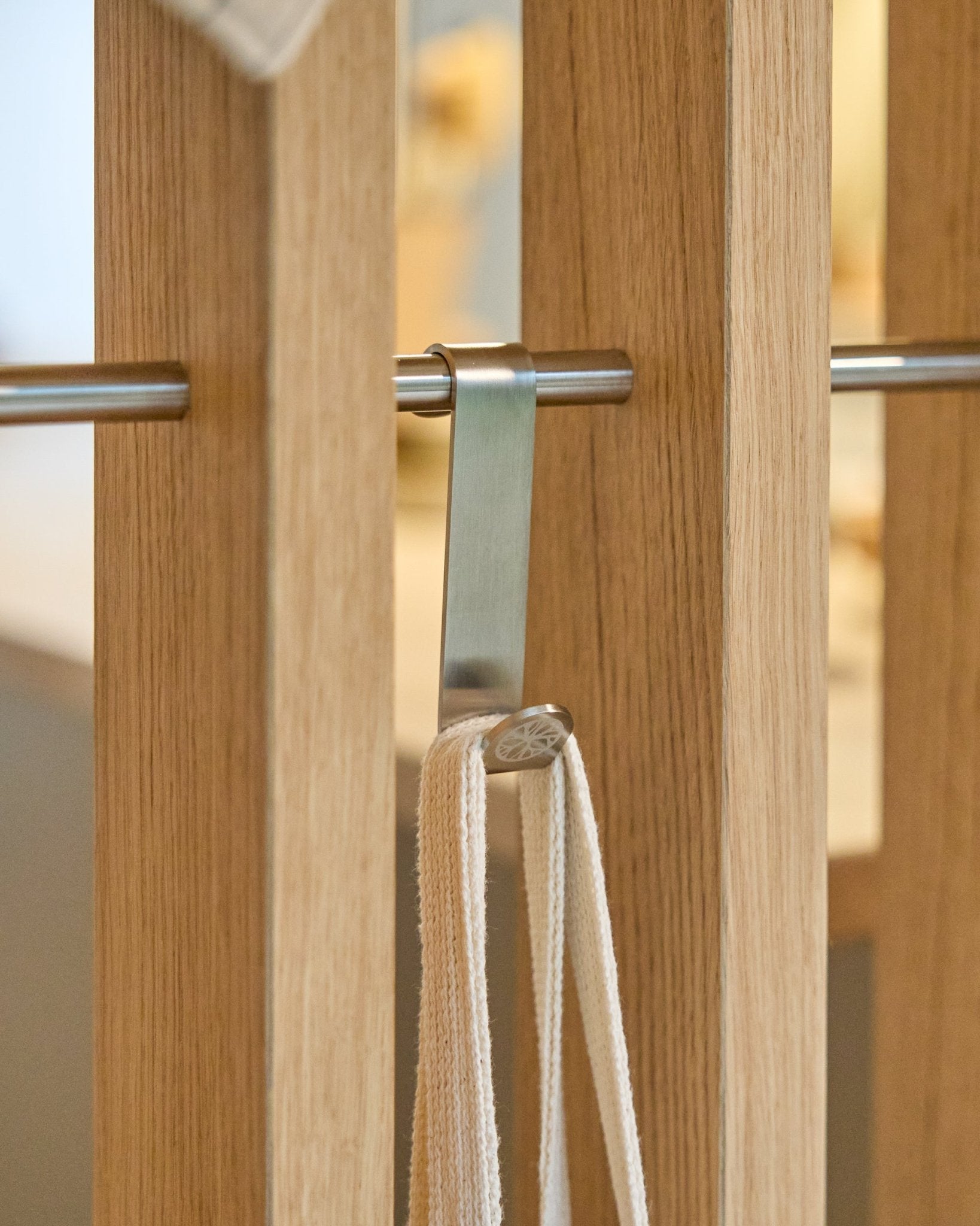 A stainless steel WoodUpp Alva S-Hook secures a beige strap to a rod mounted between vertical wooden acoustic slat panels. Set includes 2 hooks.