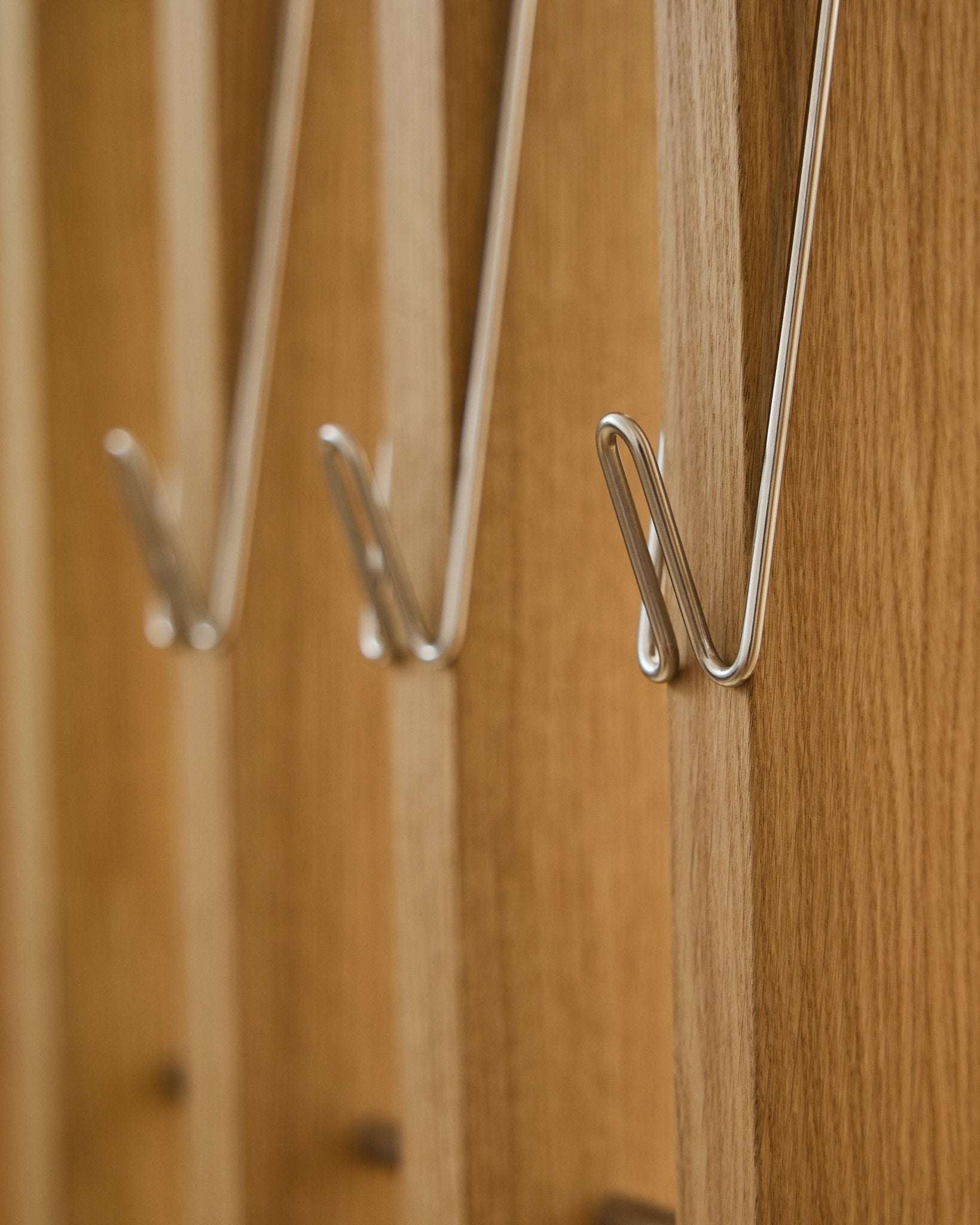 Nærbillede af tre Alva | Wire Hook / BM1, rustfrit Steel, lang fra WoodUpp, monteret på række på Akupanel akustiske træpaneler og med bløde skygger.