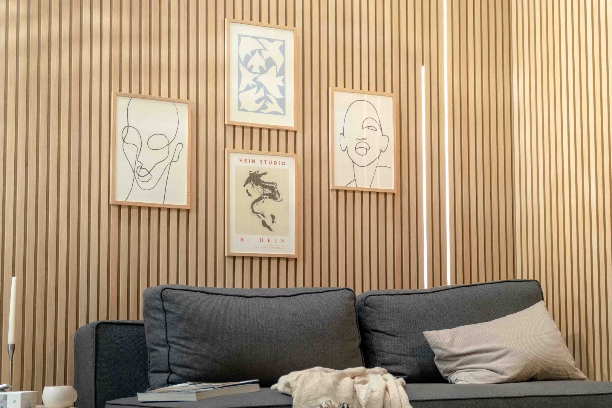 Moderne stue med en mørk sofa med en beige pude, fremhævet af en nordisk Akupanel akustisk træpladevæg og minimalistisk skandinavisk kunst ovenover.